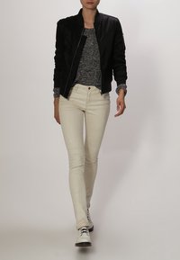 Veste bomber noire portée sur un pull gris texturé, associée à un jean skinny clair et des chaussures blanches à lacets. Design simple et moderne.