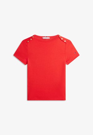 Rød T-shirt med korte ærmer, guldknapper på begge skuldre og en lille logo på venstre ærme.