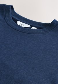 Navy blauwe crewneck trui met zichtbare witte maat- en merklabels aan de binnenzijde van de hals op een lichte achtergrond.