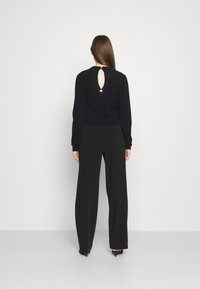 Czarny dziany sweter z dekoltem w kształcie łezki na plecach i okrągłym kołnierzem, zestawiony z czarnymi spodniami o wysokim stanie. Gładka tekstura, luźny krój.