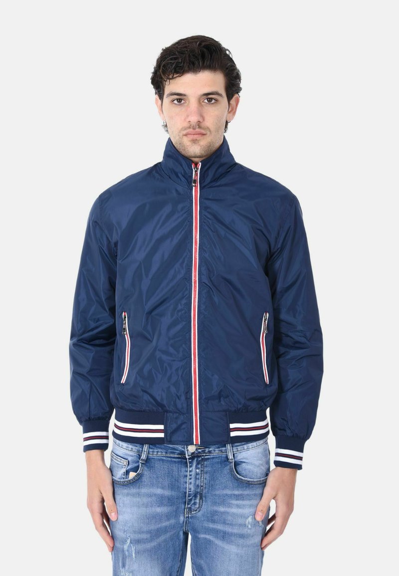 Giacca leggera della marina con colletto alto, zip frontale e due tasche con zip. Presenta accenti a strisce rosse e bianche ai polsini e all'orlo.