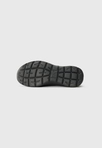 Sole of a black sneaker showing detailed tread pattern with interconnected grooves and textured grip zones on a white background.