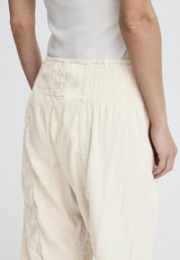 Pantalons beige clair, coupe décontractée, avec une taille smockée et une petite poche plaquée ; fabriqués à partir d'un tissu doux et texturé.