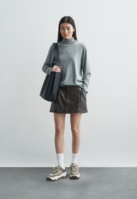 Jersey gris de manga larga con cuello alto, falda de cuero marrón con costuras, bolso negro, calcetines blancos y zapatillas deportivas gruesas con detalles marrones.