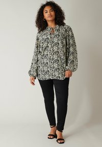 Sort blomstret bluse med bløde ærmer og en bånd-krave; båret med sorte slim-fit jeans og sorte hælede sandaler.