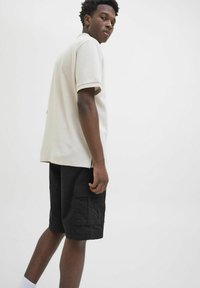 Light beige short-sleeve polo shirt with a textured fabric, paired with black cargo shorts. Notable side slits on the shirt.
