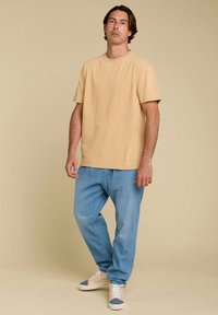 T-shirt en coton beige, coupe décontractée, associé à un pantalon en denim bleu clair. Les chaussures présentent des accents multicolores et un design classique à lacets.