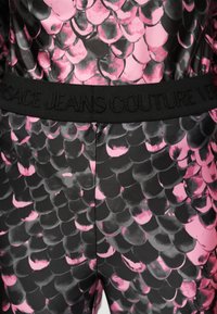 Ύφασμα με σχέδιο σε μαύρο και ροζ χρώμα με ζώνη σε μαύρο χρώμα που φέρει ανάγλυφο κείμενο "Versace Jeans Couture".