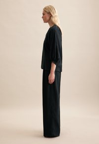 Top in lino nero con maniche a sbuffo abbinato a pantaloni larghi neri, entrambi caratterizzati da una vestibilità comoda e una superficie liscia, mostrati di lato.