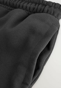 Los pantalones de chándal negros presentan un material suave de mezcla de algodón, una cinturilla elástica y bolsillos laterales con una textura lisa y costuras limpias.