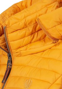 Veste rembourrée d'un orange vif, arborant un col haut, des piqûres prononcées, et une fermeture éclair avec un curseur décoratif. Détail brodé visible.