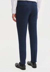 Granatowe spodnie garniturowe z teksturowanej tkaniny, o dopasowanym kroju, z tylnymi kieszeniami i gładkim paskiem w talii. Noszone z czarnymi butami wizytowymi.