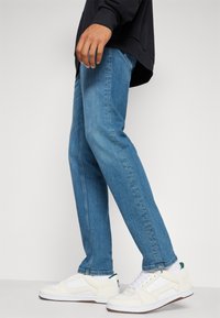 Jeans de mezclilla azul claro con corte recto, combinados con zapatillas blancas con acentos perforados y detalles en verde.