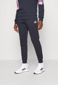 Pantalones de chándal azul marino con un ajuste ajustado, que presentan un logo blanco de Adidas y detalles en rosa en la sudadera de rayas negras. Material de mezcla de algodón.