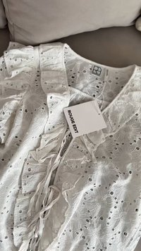Blusa bianca ricamata con dettagli arricciati e design a taglio. Presenta un'etichetta con la scritta "ROUGE EDIT" attaccata da un cordoncino.