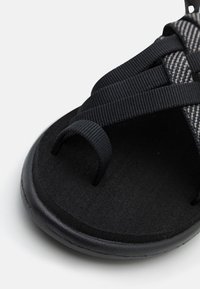 Svart sandal med en texturerad fotbädd, grårandiga remmar och en slät gummisula med en tåslits för en säker passform.