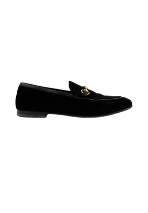 Zwarte suède loafer met lage hak en gouden metalen horsebit-detail bovenop, zijaanzicht op witte achtergrond.