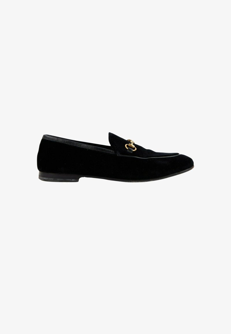 Mocassin en daim noir avec petit talon et détail en métal doré en forme de mors de cheval sur le dessus, vu de profil sur fond blanc.