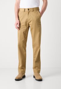 Beige chinos with a straight-leg design, made from a smooth fabric. Features a button closure and front pockets, paired with beige boots.