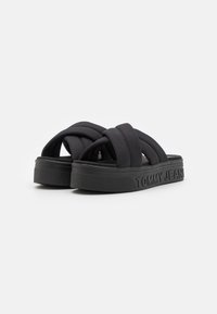 Chanclas negras de tiras elásticas cruzadas, suela de goma texturizada y marca en relieve "TOMMY JEANS" en el lateral. Diseño plano.