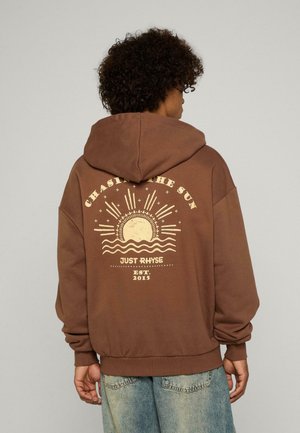 Brauner Kapuzenpullover mit einem großen Grafikdruck auf der Rückseite, der eine Sonne und Wellen zeigt. Lockerer Schnitt und gerippte Bündchen, aus weichem Material gefertigt.