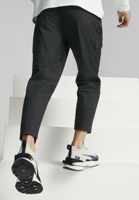 Pantalones cargo negros con piernas ajustadas, que presentan bolsillos laterales, combinados con zapatillas grises y negras que muestran una suela texturizada y acentos en el talón.