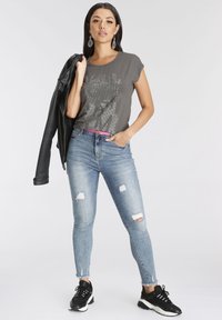 Siva grafična majica s kristali, kavbojski jeans s raztrganimi pasti, črna usnjena jakna, črni superge in roza pas.