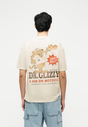 Inimene, kes kannab beežikat T-särki, millel on joonistatud koer arstina, kes hoiab hot dogi, ning teks "Feelin’ Hangry? Dr. Glizzy 1-800-DR-HOTDOG" seljal.