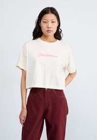 Gräddfärgad, kortärmad t-shirt i mjuk bomull med rund halsringning, med en rosa "Nike Sportswear"-logotyp i mitten.
