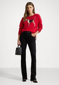 Rød genser med en brodert hundedesign, kombinert med svart flagrende jeans. Svart håndveske og spiss tå-hæler fullfører looken.