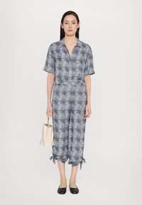Blå och vit mönstrad jumpsuit med krage, korta ärmar och knytbara avslut. Kombineras med en ljusbeige handväska och svarta ballerina. 