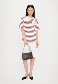 Stribet t-shirt med en lomme, parret med hvide shorts. Sort lædertaske med struktureret design. Spidse sorte sko.