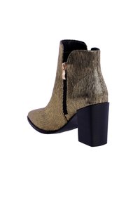 Botín de tobillo texturizado en dorado con tacón cuadrado, cierre de cremallera lateral y diseño acanalado. La suela es negra, realzando el contraste general.