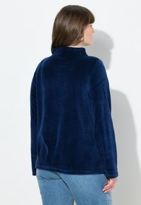 Sudadera de forro polar azul marino con cuello alto, mangas largas y una textura suave. La parte posterior muestra un ajuste relajado y detalles de diseño mínimos.
