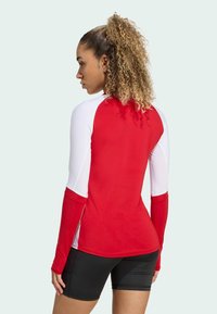 Maglietta a maniche lunghe da surf con corpo rosso e maniche bianche, tessuto testurizzato sulle spalle e vestibilità sportiva. Abbinata a pantaloni shorts neri.
