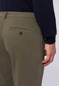 Olivgröna chinos med en mjuk textur, har en bakficka med knappstängning och subtila broderidetaljer.