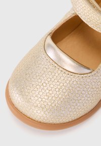 Goldfarbene, texturierte Leder-Mary-Jane-Schuhe mit einem glänzenden, metallischen Riemen und einer glatten, hellbraunen Sohle. Einzigartiges Wabenmuster auf der Oberfläche.