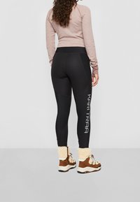 Svarta leggings med geometrisk panelering, med en grå logotyp på vänster ben, i kombination med bruna och krämfärgade stövlar med foder av päls.