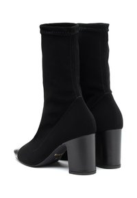Botas negras de tobillo con parte superior de tela suave, tacón estructurado y puntera brillante. Presenta un puño cosido y un diseño de tacón cuadrado.