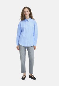 Light blue, long-sleeve button-up shirt with vertical white stripes, paired with gray jeans and black flat shoes. Features a spread collar and relaxed fit.