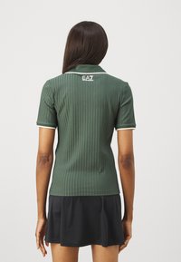 Zelený pruhovaný polo tričko s krátkymi rukávmi, bielym lemovaním a logom na chrbte; v kombinácii s čiernym skortom.