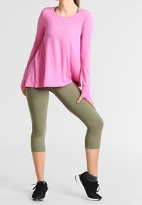 Haut rose à manches longues avec une coupe ample, associé à des leggings capri verts olive et des chaussures de sport noires avec une semelle texturée.