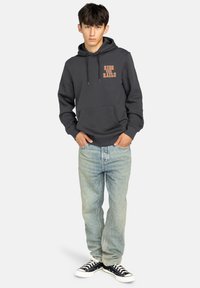Sudadera gris oscuro con un bolsillo frontal y texto naranja "RIDE THE RAILS", combinada con vaqueros azul claro y zapatillas negras.