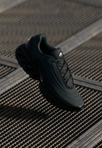 Black athletic sneaker featuring a textured surface, rounded toe, thick sole with visible air cushioning, and prominent lacing system.