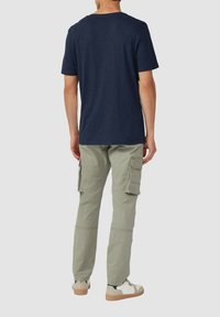 Granatowa koszulka z okrągłym dekoltem w połączeniu z jasnoniebieskimi spodniami cargo z bocznymi kieszeniami oraz beżowymi butami sznurowanymi z teksturowaną podeszwą.