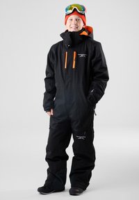 Zwarte overall met oranje accenten, ritszakken en een capuchon. Het model draagt een bril en een rode muts. Duurzaam en functioneel ontwerp.