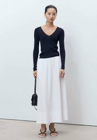 Marinblå ribbad långärmad topp och en vit, flödande maxikjol. Modellen håller en liten svart handväska. Minimalistisk med en avslappnad passform.