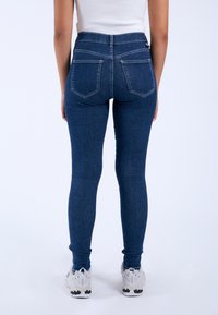 Blue skinny jeans made of denim, featuring a high waist, two back pockets, and a simple design. Worn with white athletic shoes.