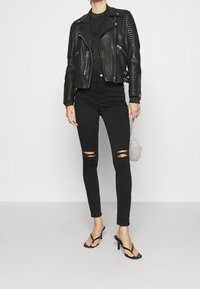 Czarna skórzana kurtka motocyklowa z prążkowanymi ramionami, czarny sweter o fakturze, podarte czarne obcisłe dżinsy oraz czarne sandały na obcasie z paskami.