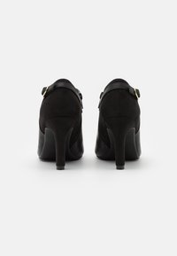 Czarne szpilki z zamszowej góry, skórzanymi akcentami, wysokim obcasem typu stiletto oraz regulowanymi paskami na kostkę z złotymi detalami.